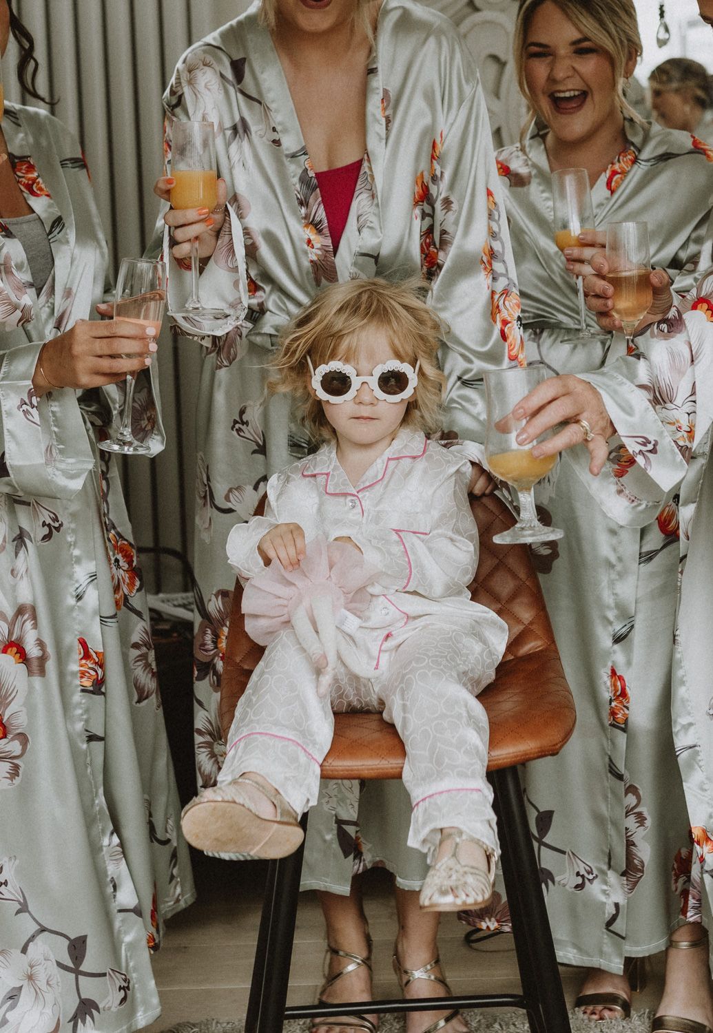 Group wearing floral silk robes toasting with champagne glasses during pre-wedding celebration.