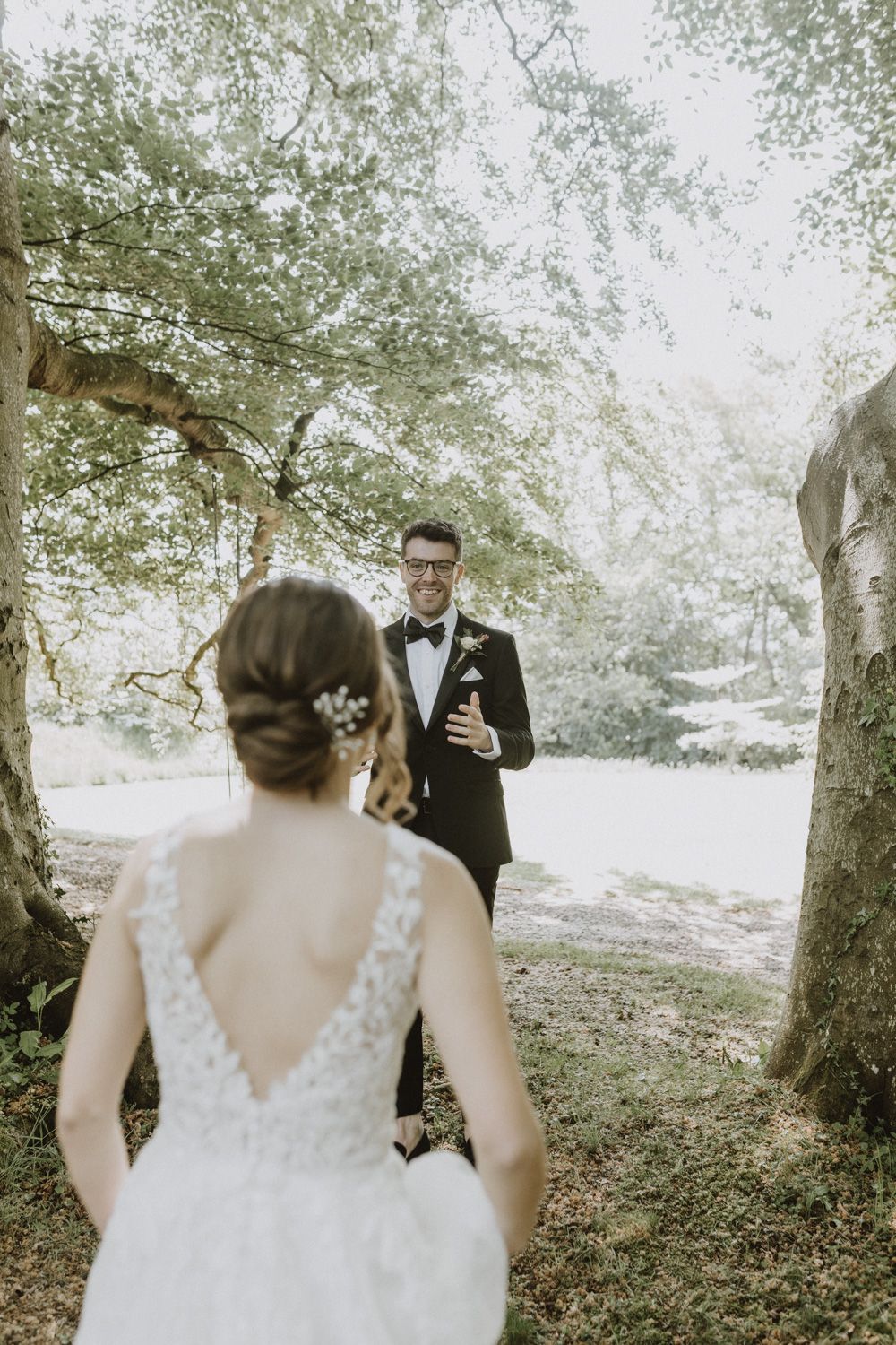 First look wedding moment captured in a sun-dappled wooded setting.