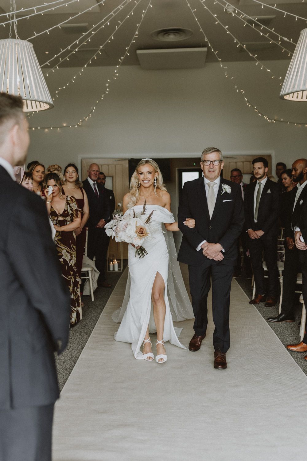 Wedding ceremony in a venue decorated with string lights and white lampshades.