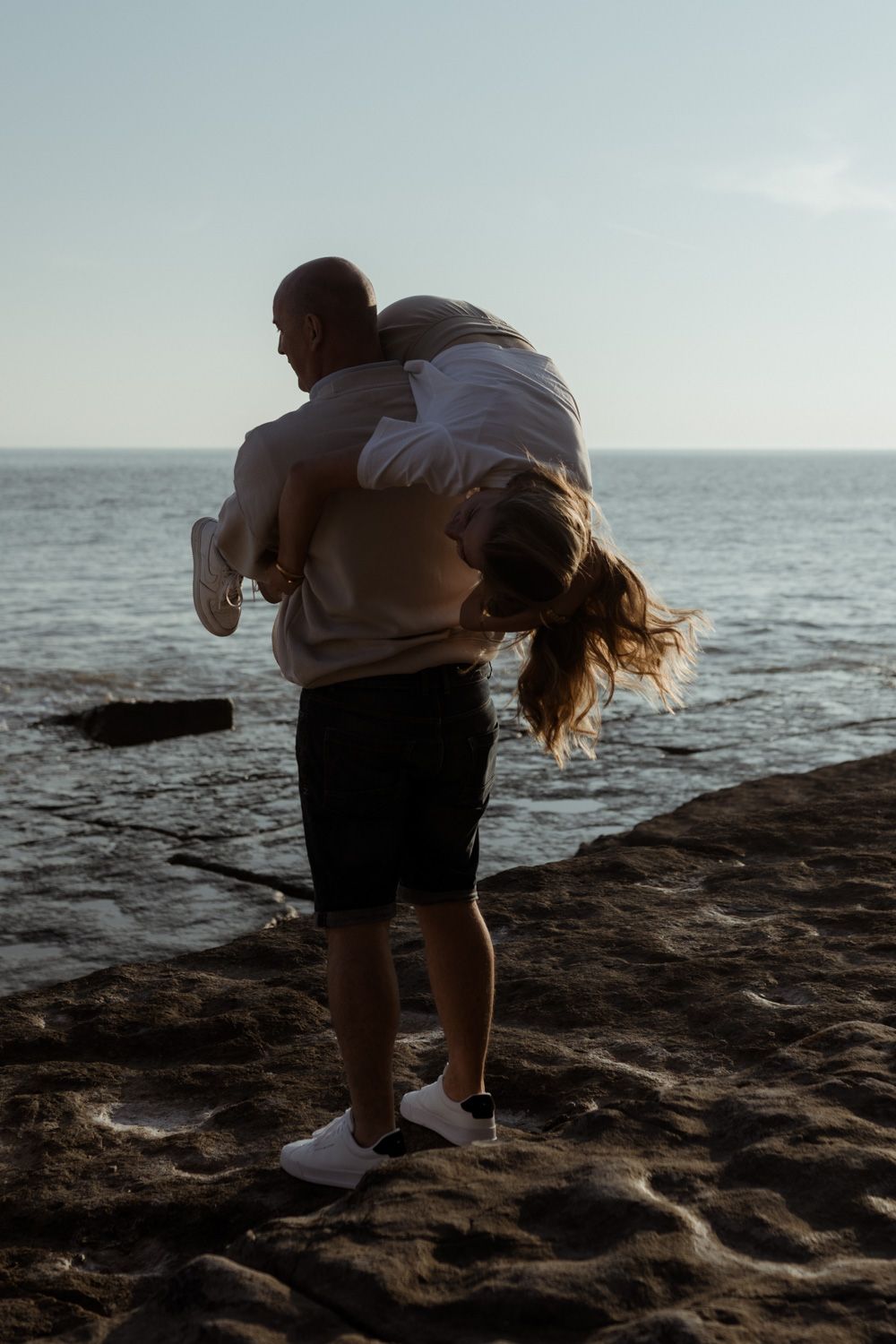 Playful moment captured between two people on rocky ocean shore.