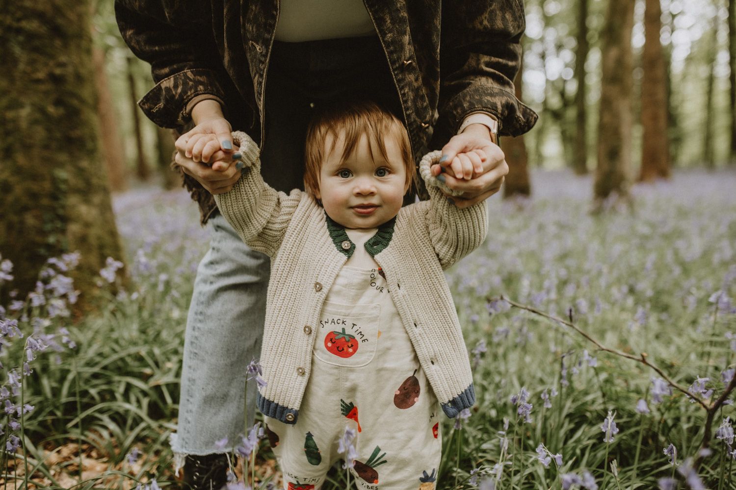 Figure holds a fresh purple wildflower in a dreamy spring woodland filled with blooming bluebells.
