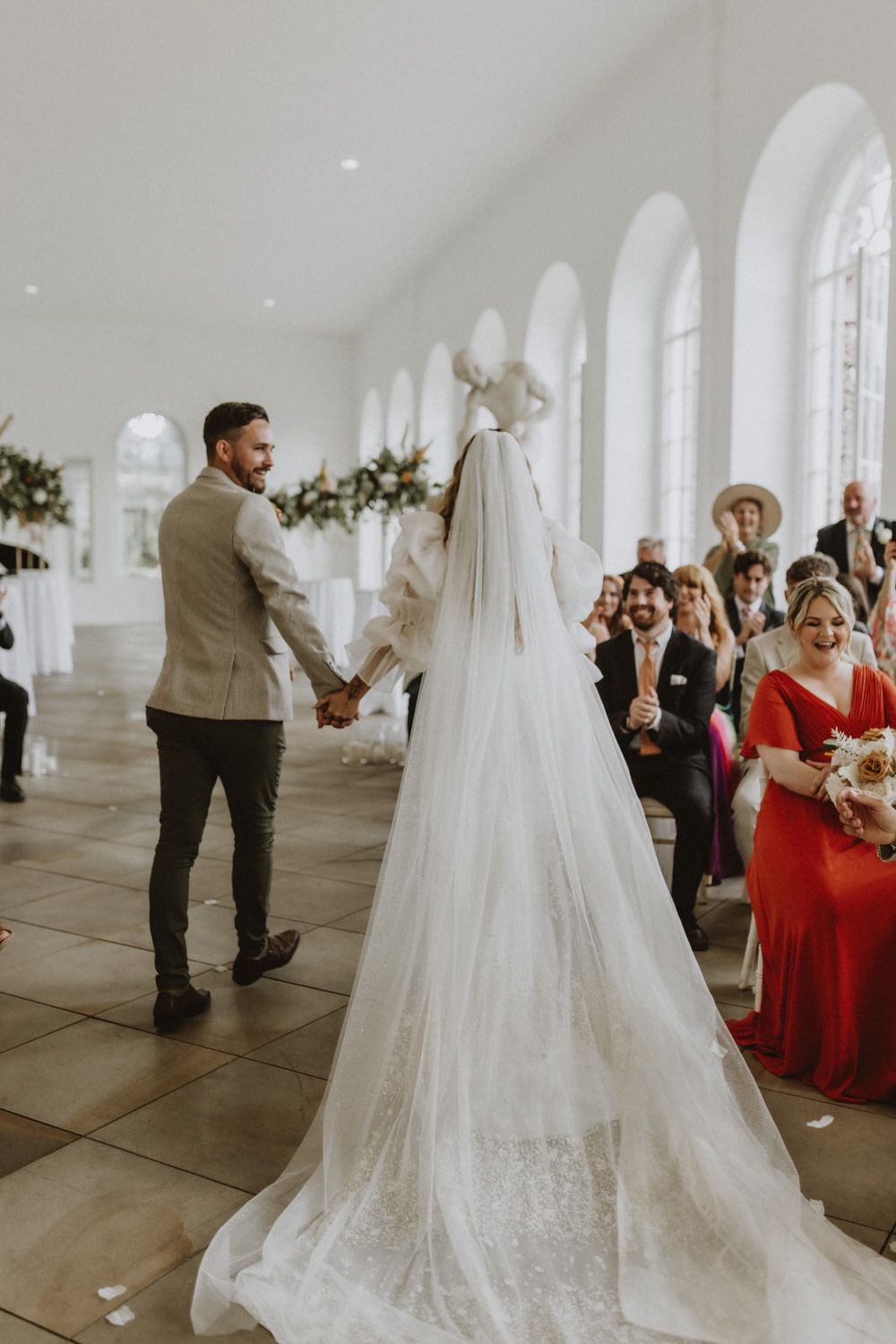 Elegant wedding ceremony in a bright white chapel with arched windows and guests watching the couple exchange vows.