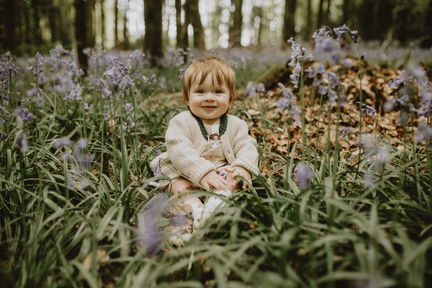 Little one playing in blooming forest floor surrounded by purple wildflowers.