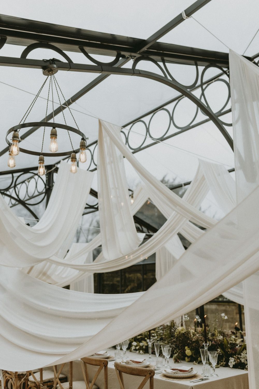 Elegant white fabric draping beneath vintage chandeliers creates a romantic wedding reception atmosphere.