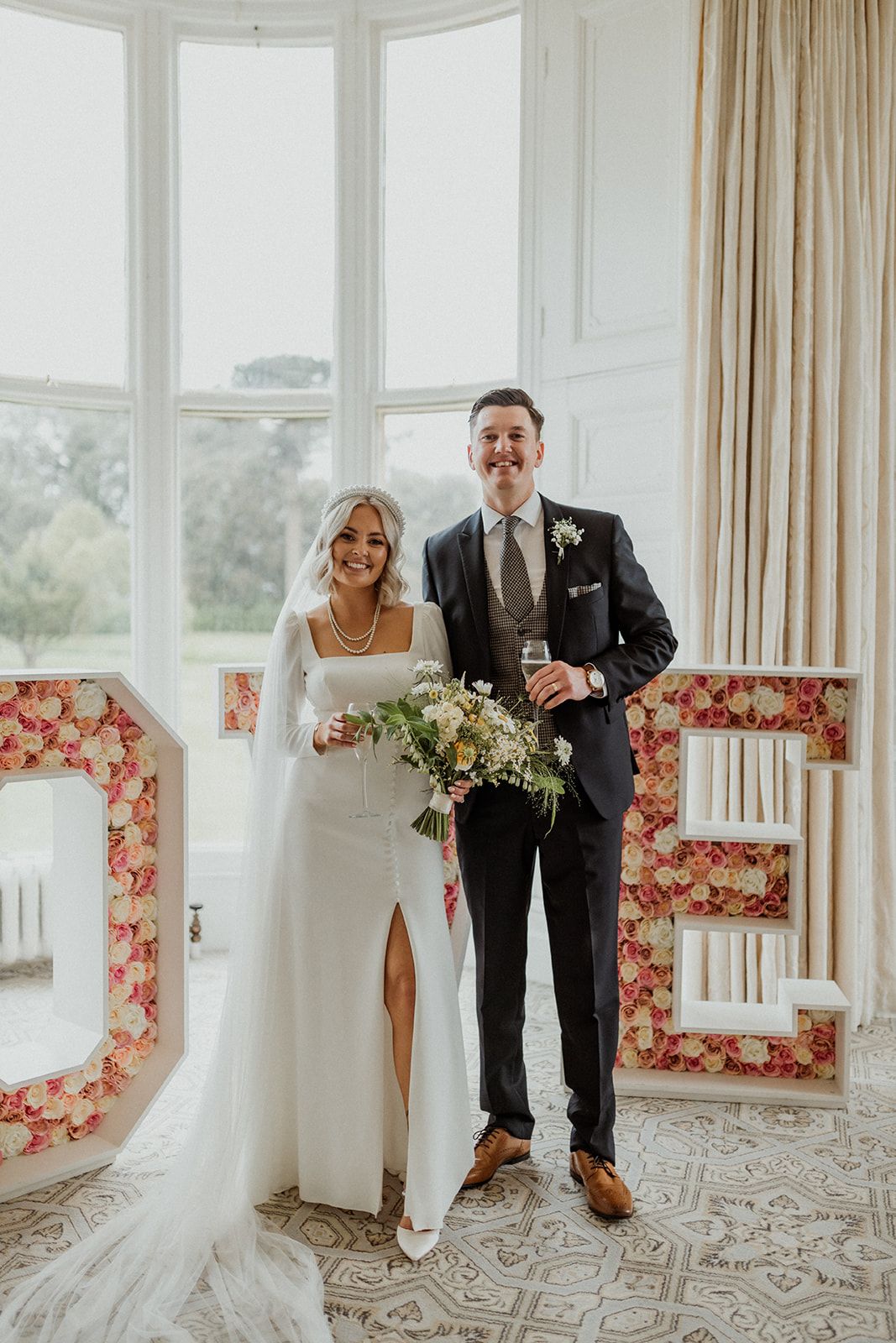 Wedding couple shares candid laughing moment in bright sunlit room with floral-patterned window seating.
