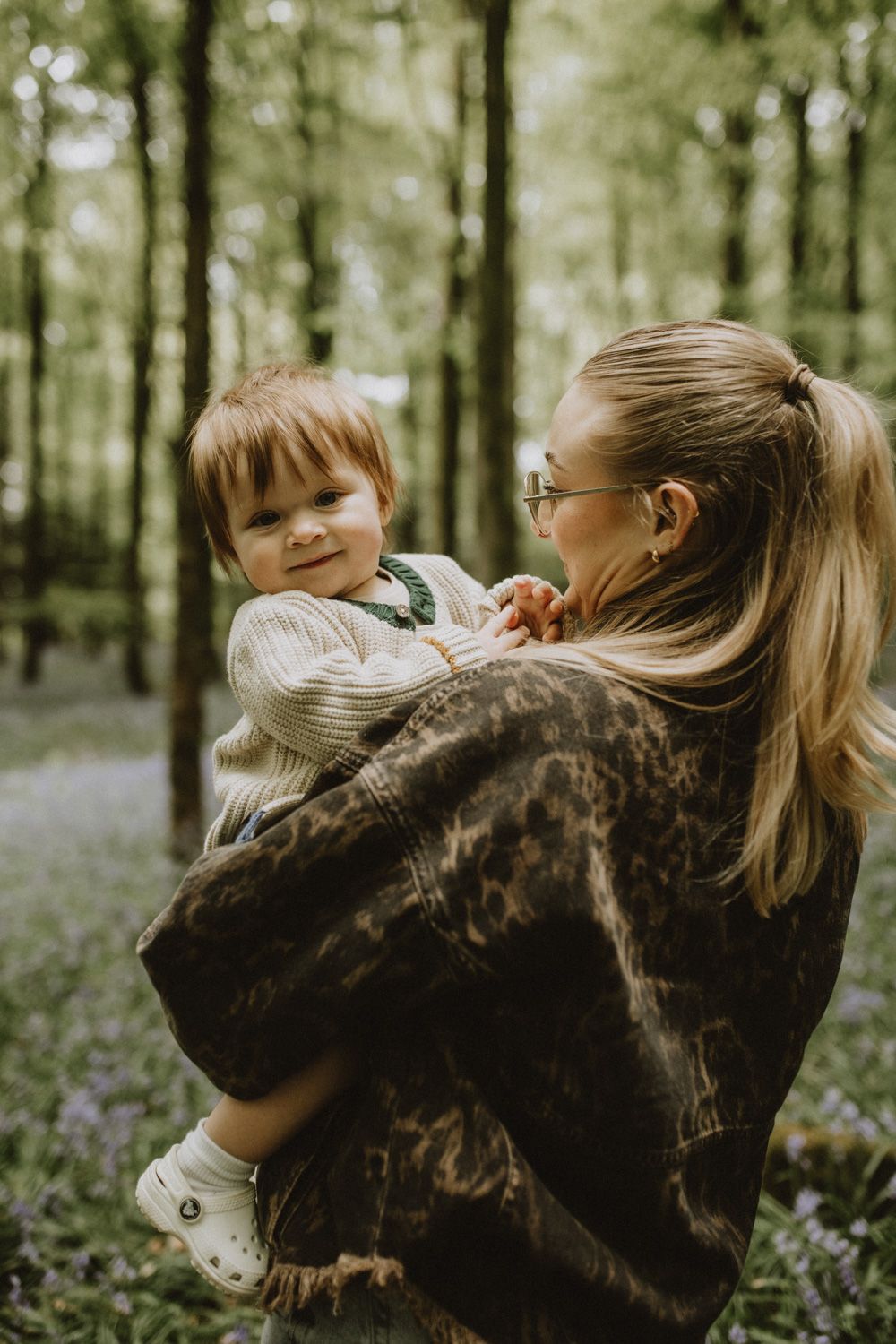 Candid family moments captured in a sunlit forest with blooming bluebells.