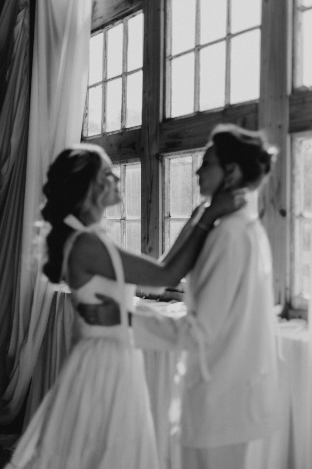 Two figures in white clothing dancing near a window in a romantic black and white scene.