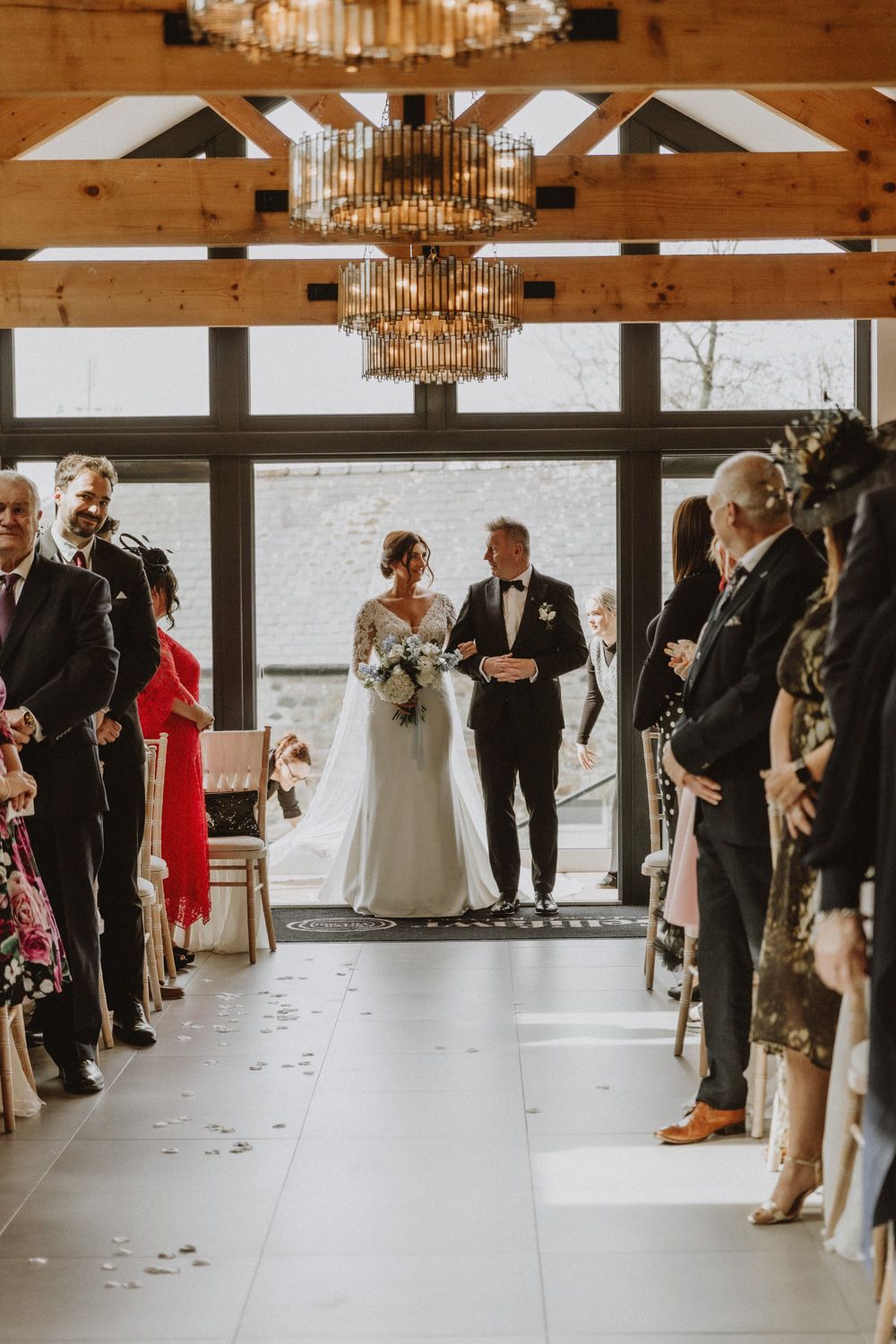 Wedding ceremony in modern rustic venue with wooden beams and crystal chandelier.