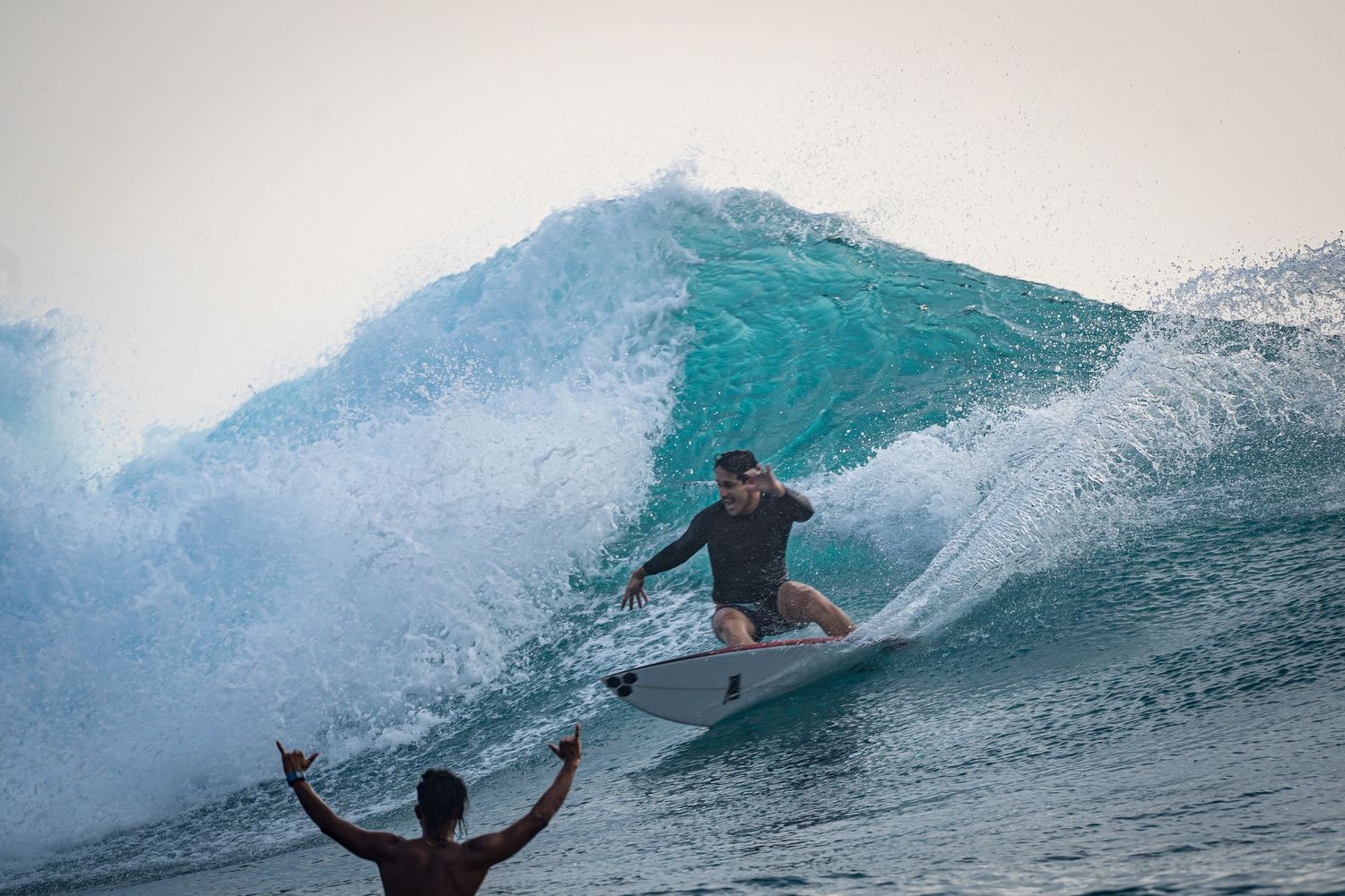 Surfer catching air on blue wave while friend throws arms up in celebration – CK Surf