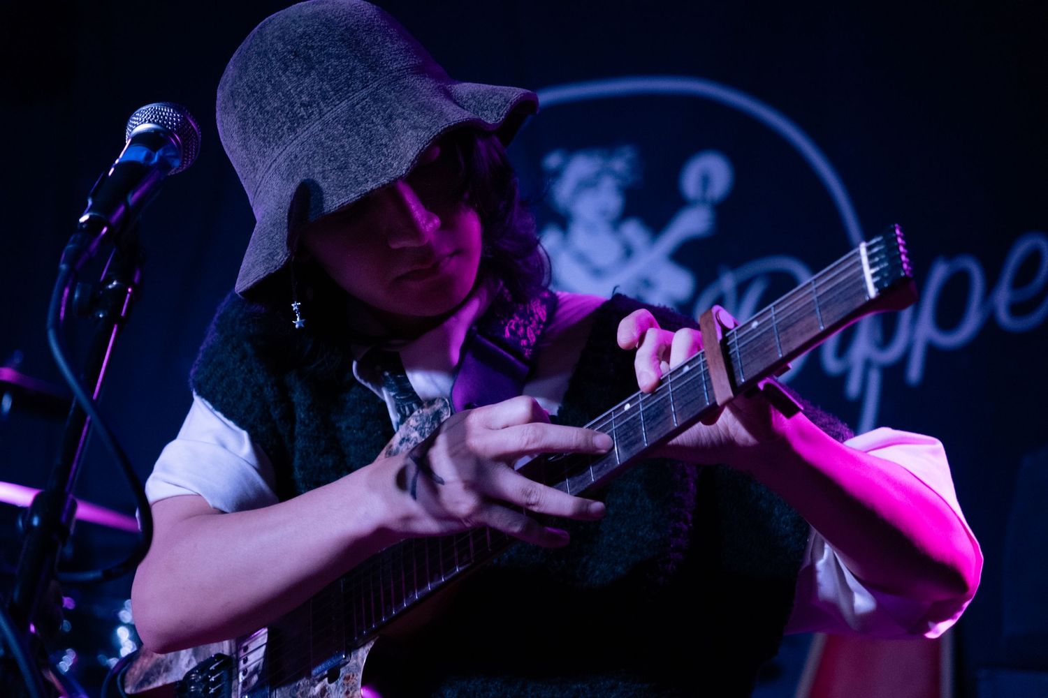 Musicians perform on stage with guitars under dramatic pink and blue lighting during a live concert performance.