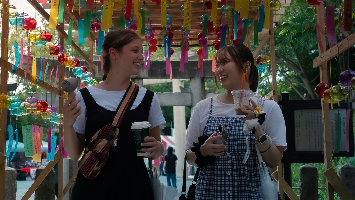 People gather under colorful paper decorations at an outdoor event with festive banners strung overhead.