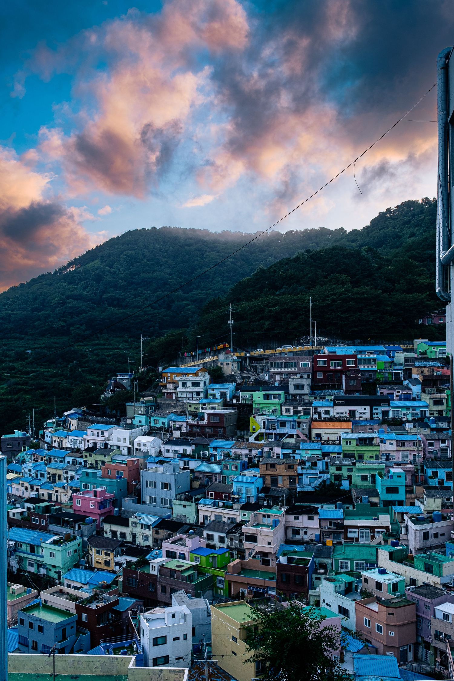 Colorful hillside village with densely packed houses against mountain backdrop during dramatic pink sunset.