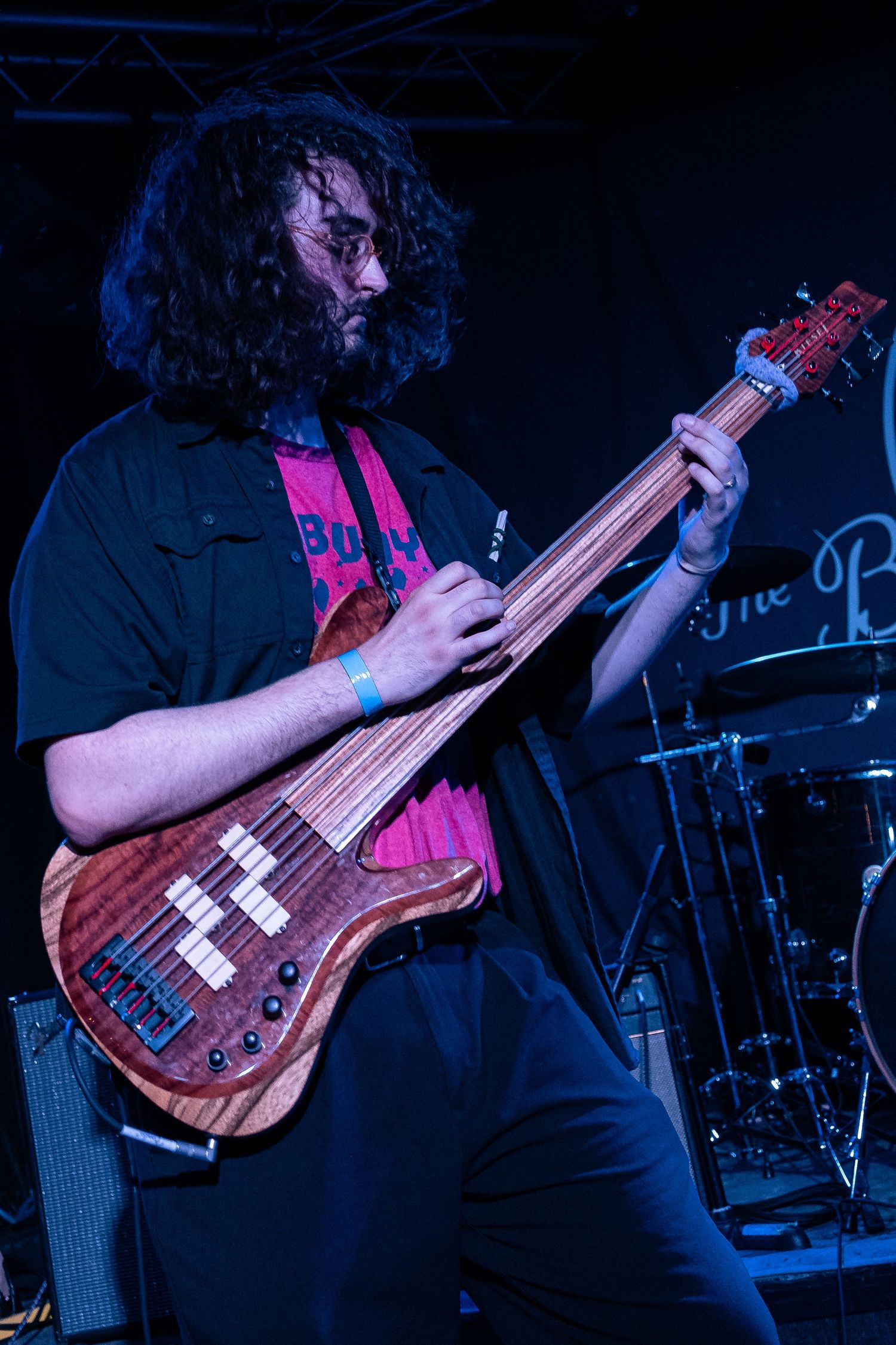 Bass guitarist performs on stage with wooden bass guitar in dark concert lighting.