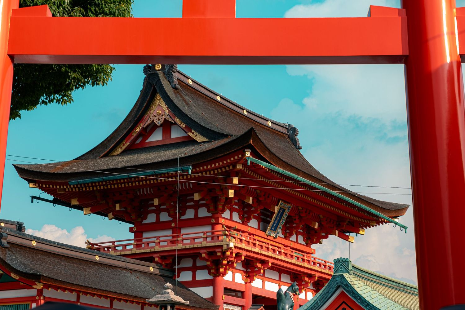 Red torii gates and traditional buildings at Fushimi Inari Shrine in Kyoto, Japan against a blue sky.
