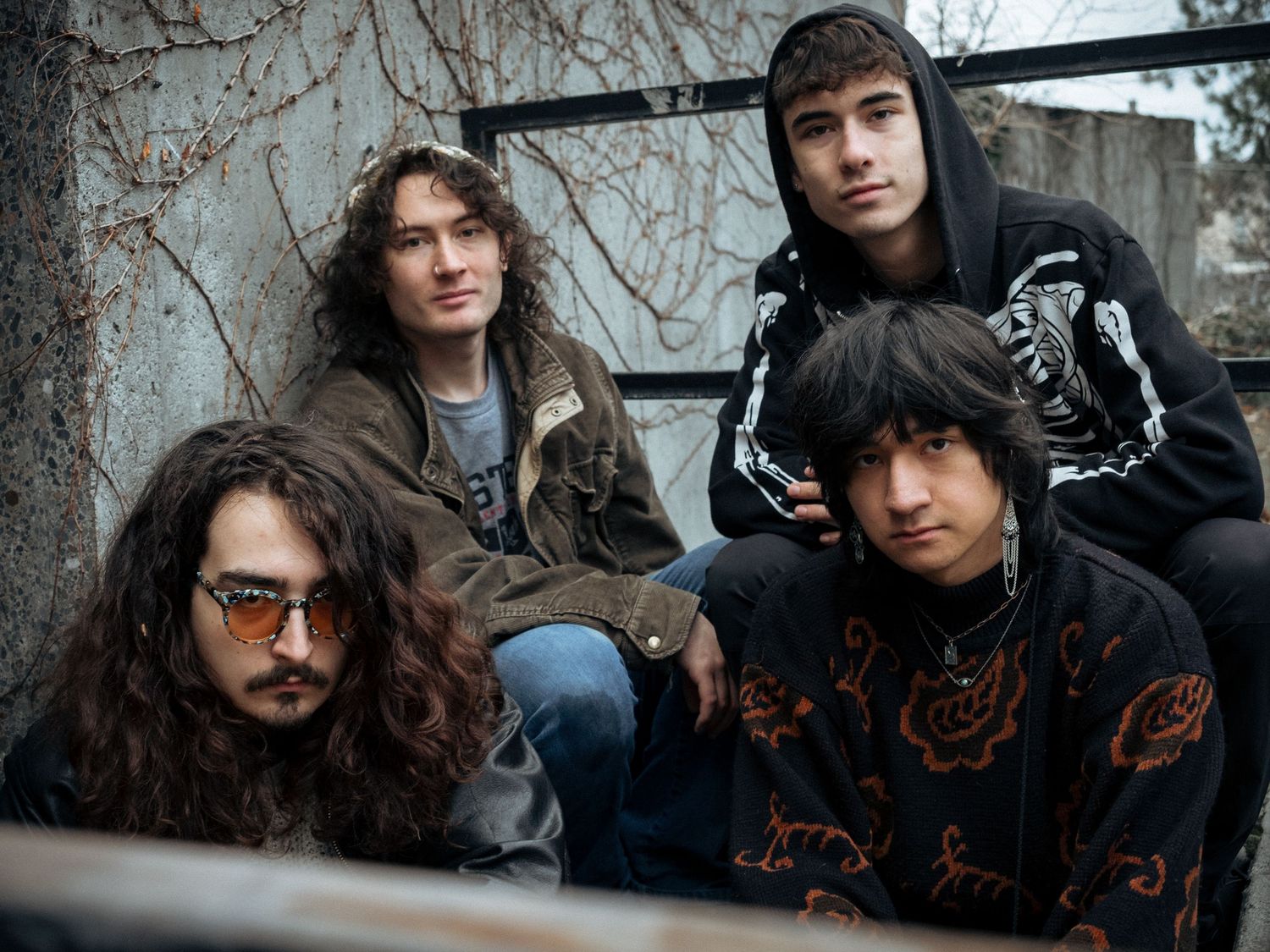 A group of young musicians in casual clothing pose together outdoors against a weathered wall.