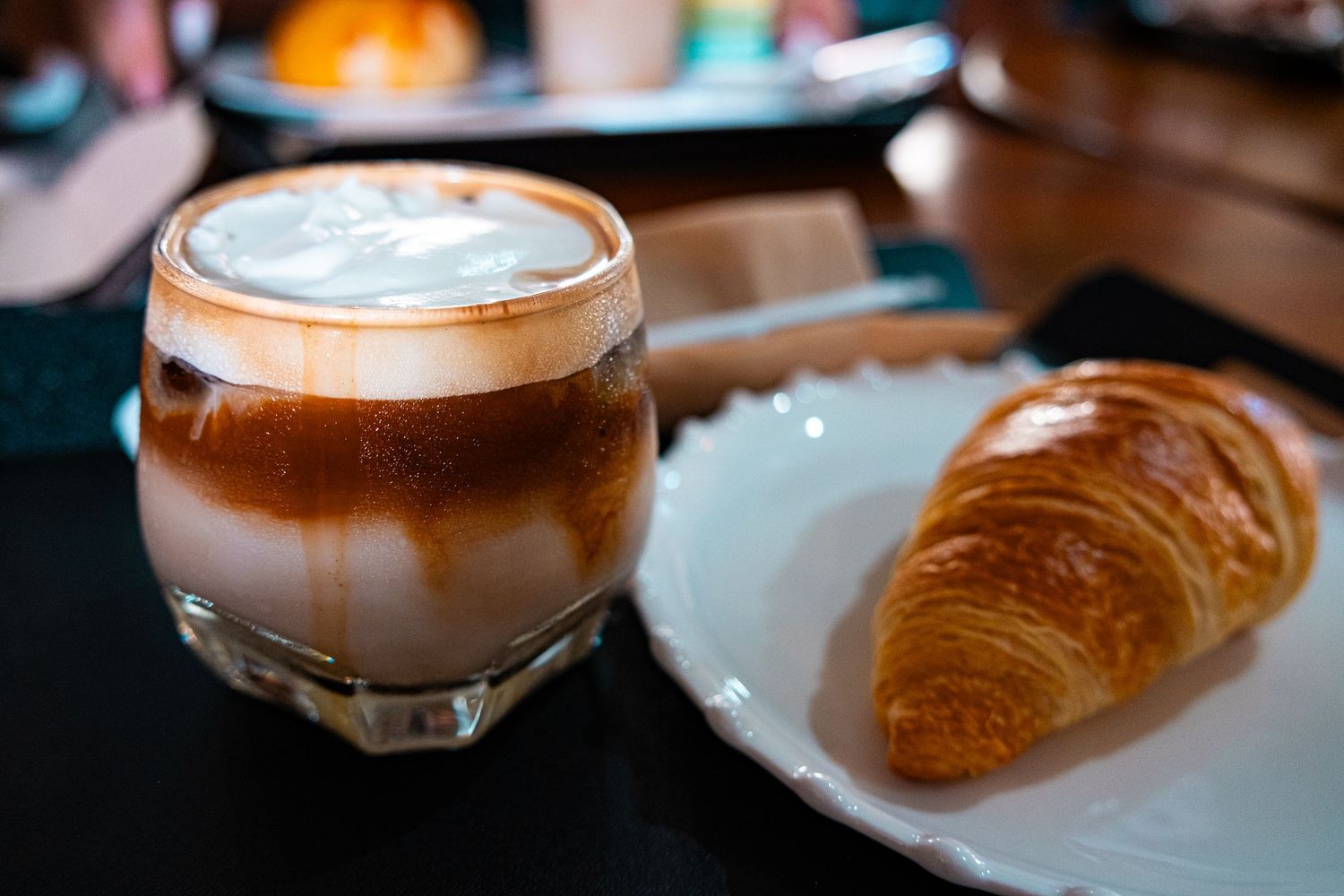 Coffee and pastries arranged in a cozy cafe setting with warm lighting and foam art.