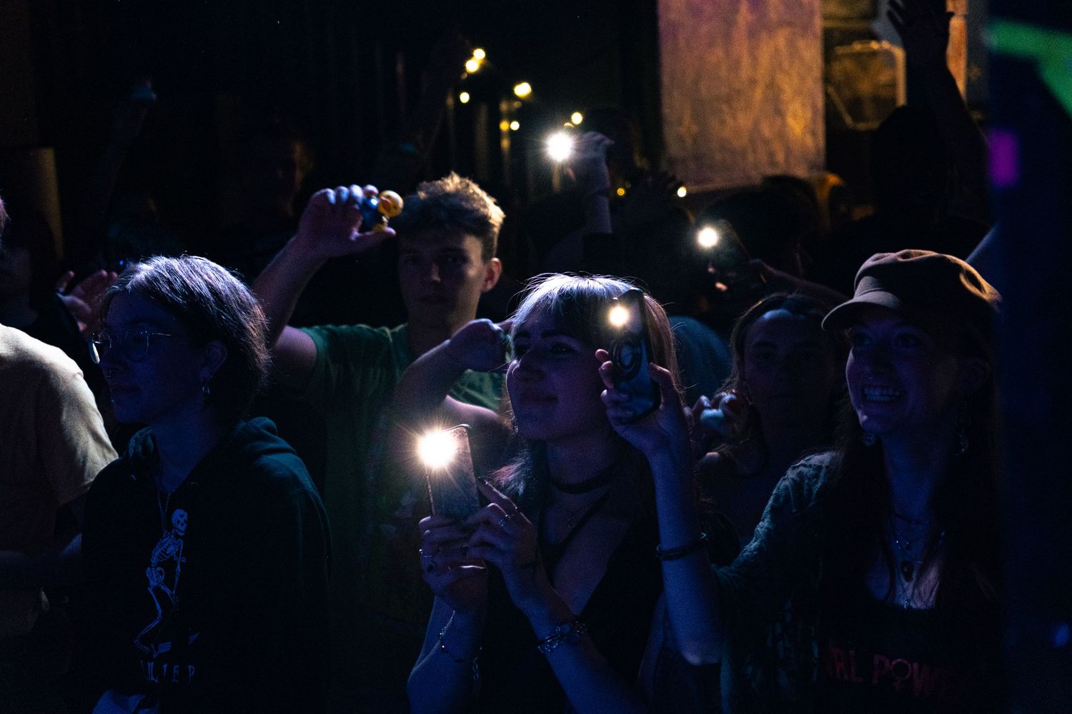A crowd of people gathered in darkness with glowing lights and illuminated faces in a nighttime scene.