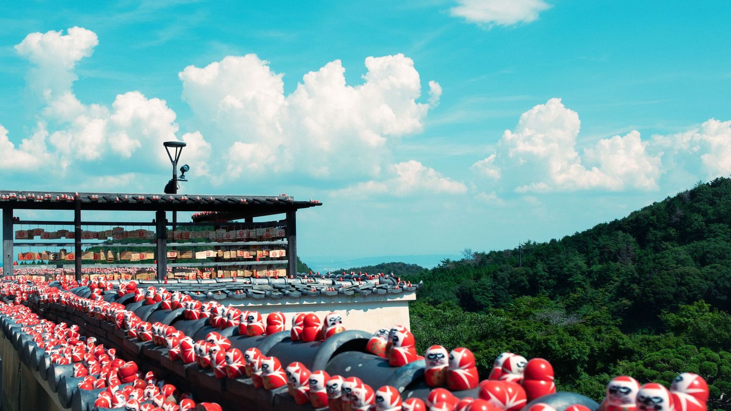 A row of red and white seats at an outdoor stadium overlooks mountains and blue sky with puffy clouds.