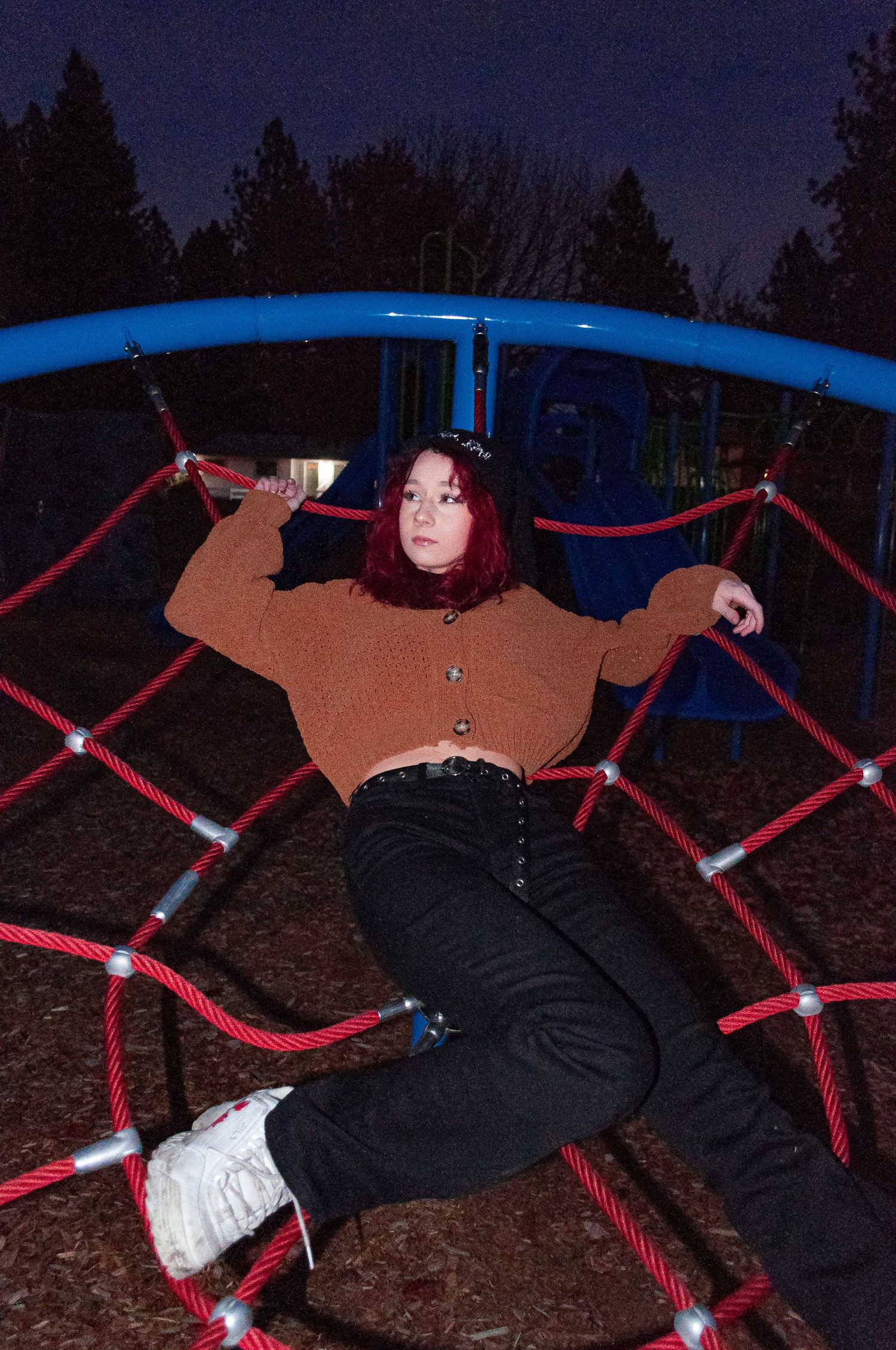 A person lies on a red and blue playground climbing structure at night under a dark sky.
