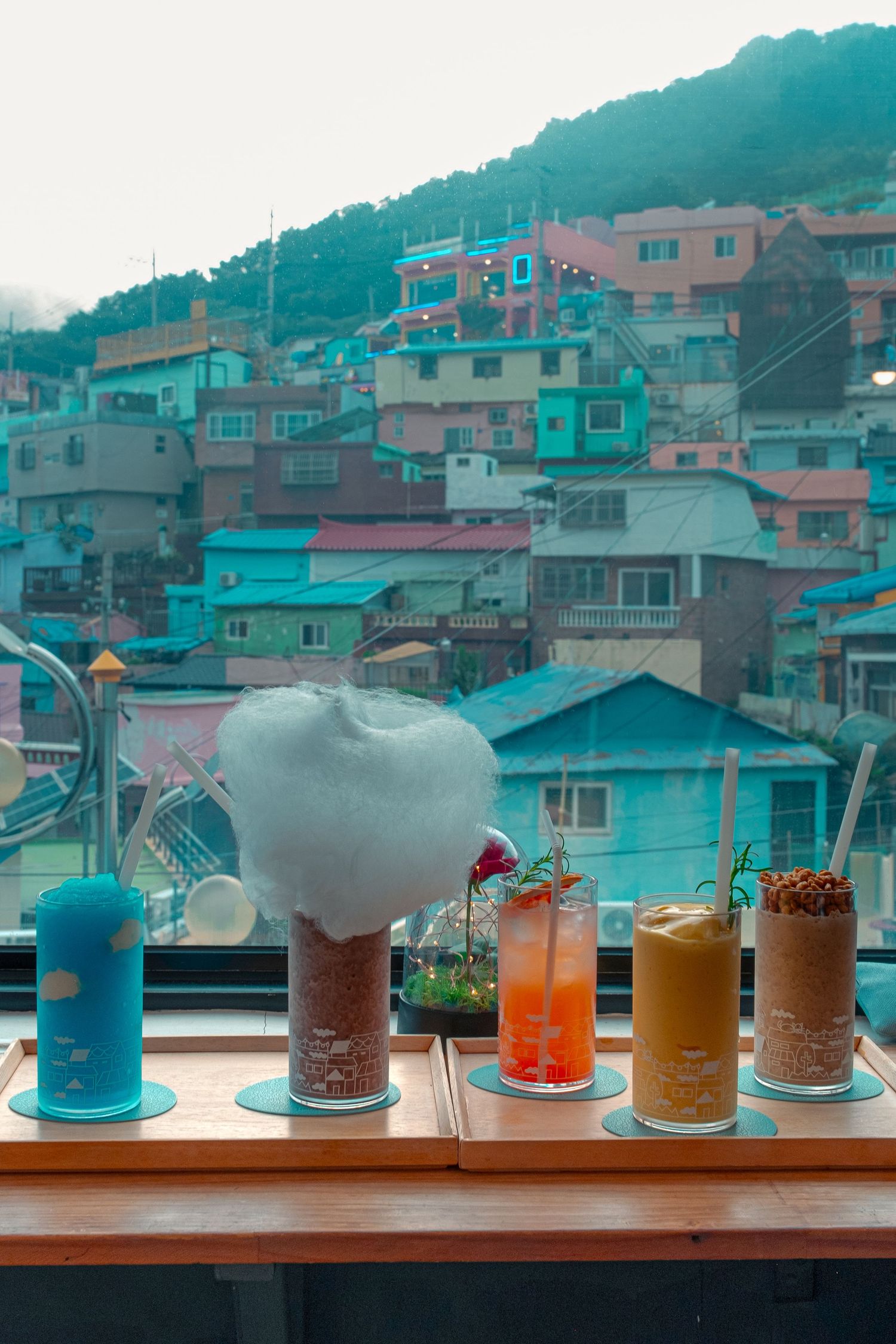 Colorful drinks arranged in front of vibrant pastel-colored hillside buildings in Korea.