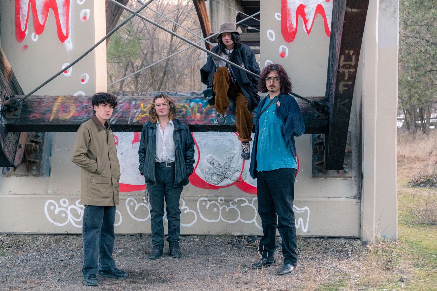 Group of people stand near graffiti-covered walls under a bridge or overpass structure.