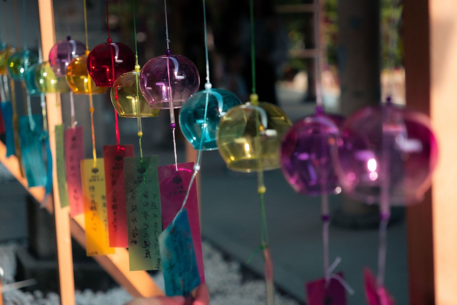 Vibrant purple and blue glass wind chimes sway in front of traditional Japanese temple buildings.