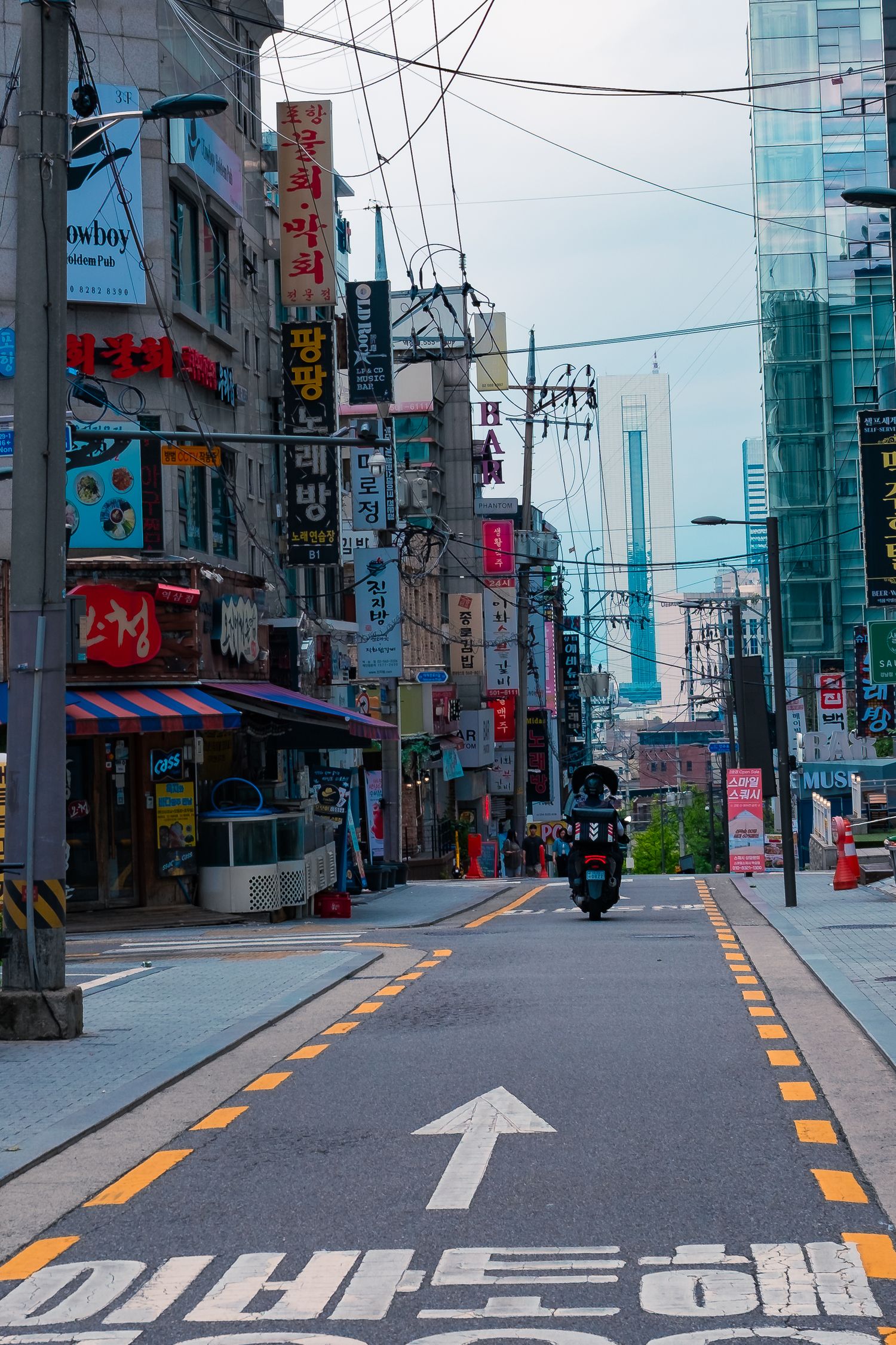 Urban street view in South Korea with directional arrows painted on an empty road and utility poles.
