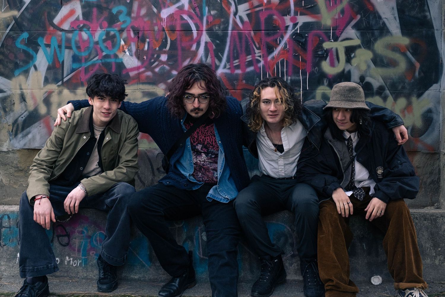 A group of people pose casually against a graffiti wall in an urban setting wearing casual winter attire.