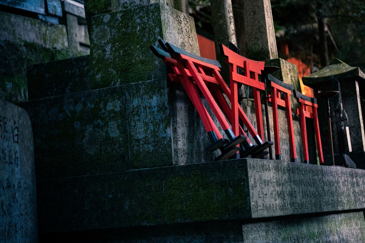 Red torii gates line a winding path through a traditional Japanese shrine at dusk.