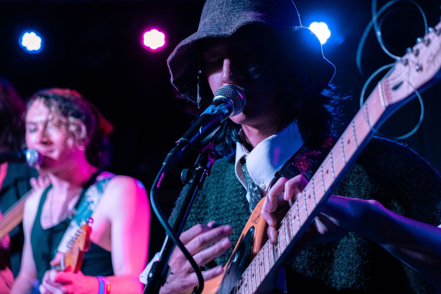 Concert performers on stage with colorful blue and pink lighting creating an energetic live music atmosphere.