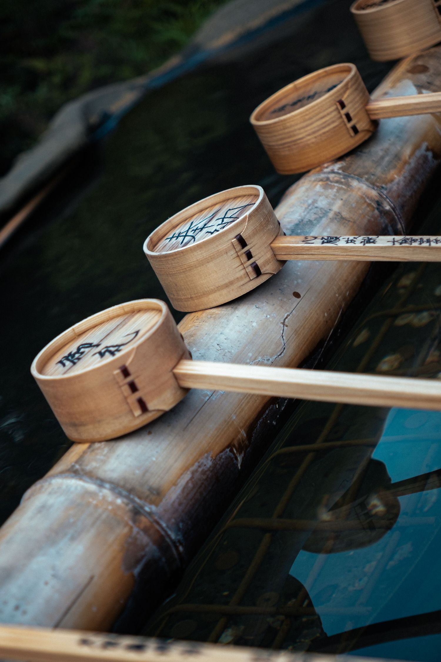 Wooden bamboo steamer baskets arranged in a row on a dark reflective surface with dramatic lighting.