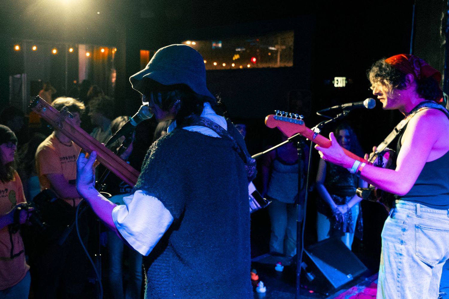 Musicians perform on a dimly lit stage with colorful lights creating an atmospheric concert environment.
