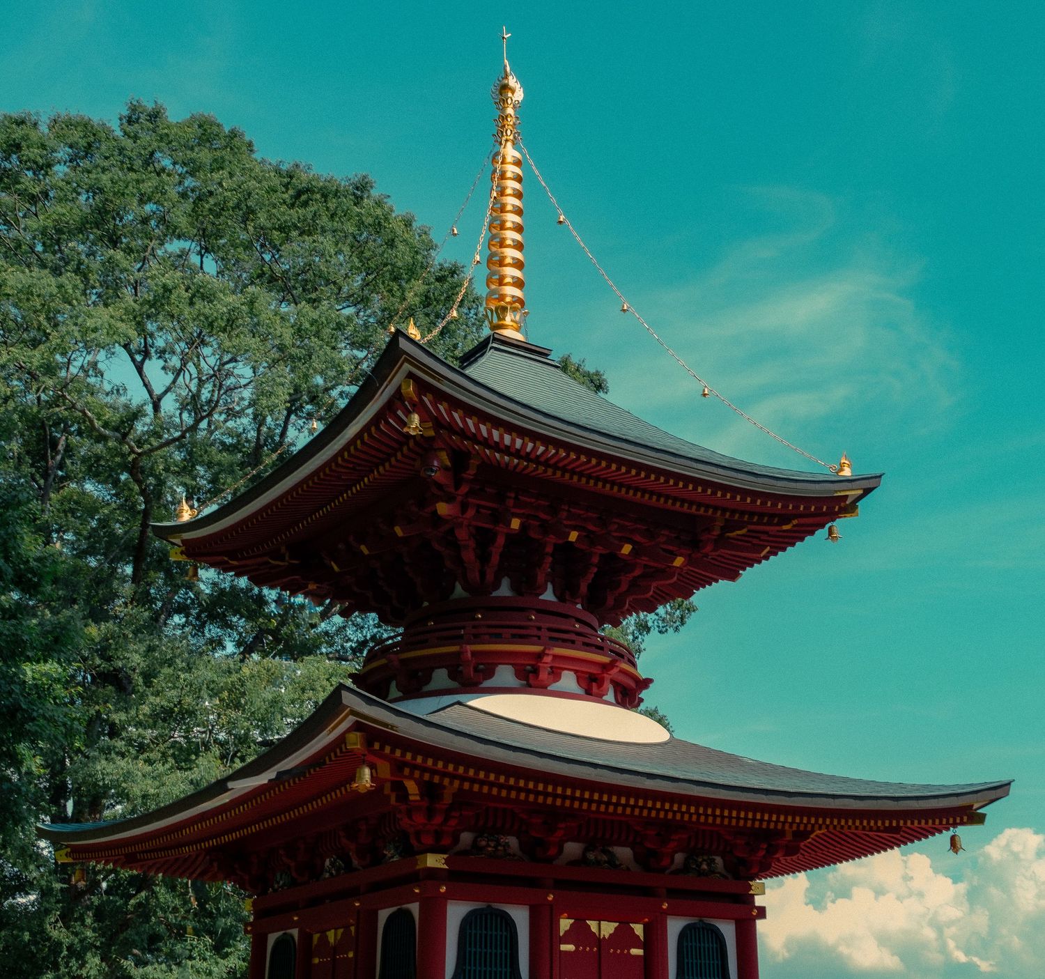 Traditional Japanese pagoda with ornate red and gold architecture against a vibrant turquoise sky on a sunny day.