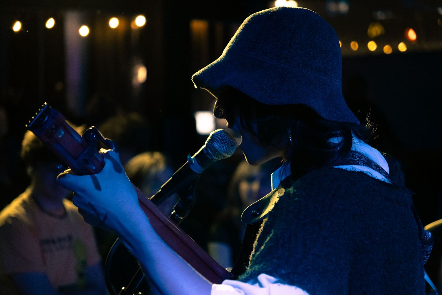 Silhouette of a performer in a bucket hat singing into a microphone at a dimly lit nighttime venue.