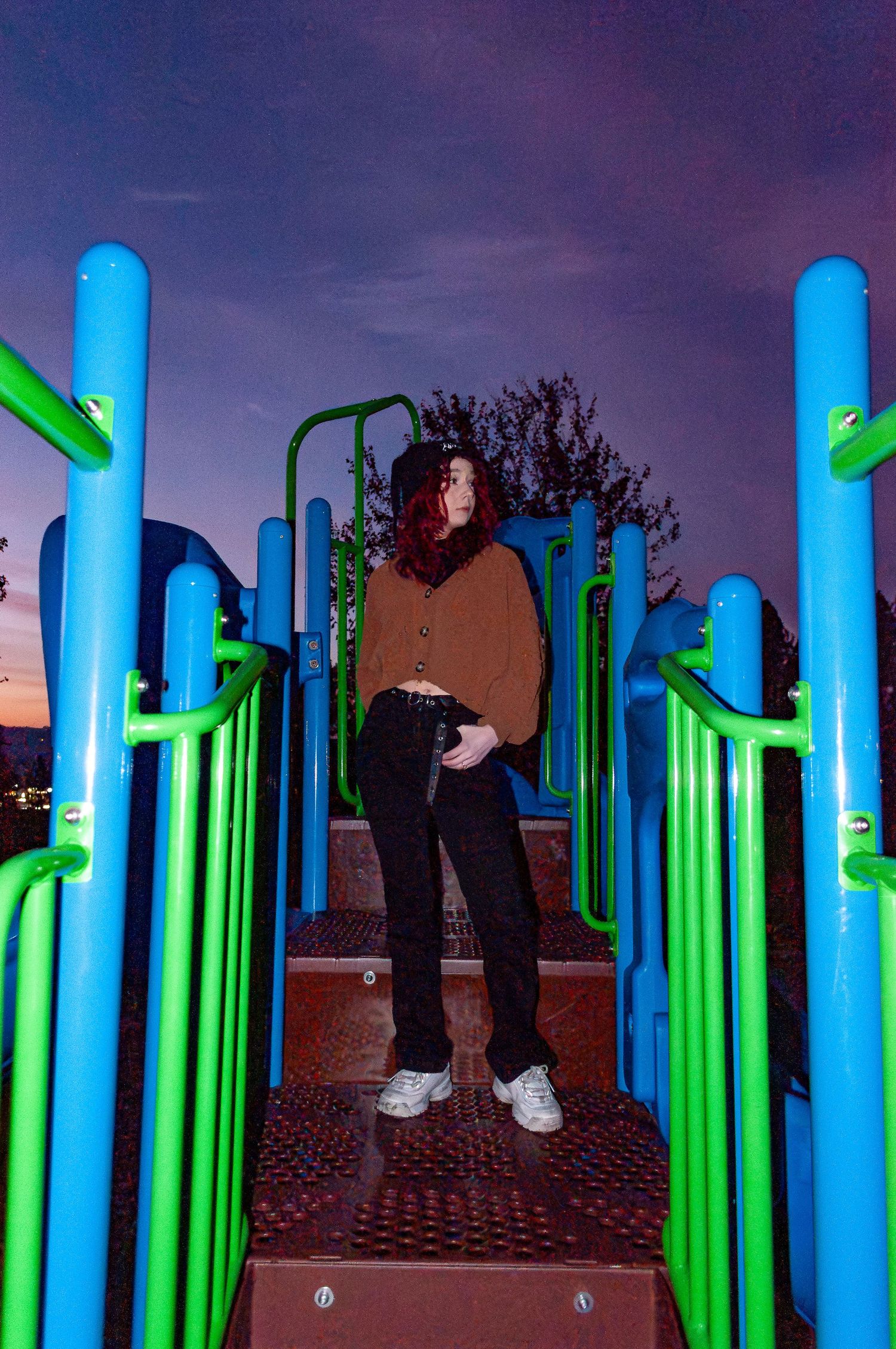 Illuminated blue and green cylindrical art installation creates a forest-like environment at dusk.