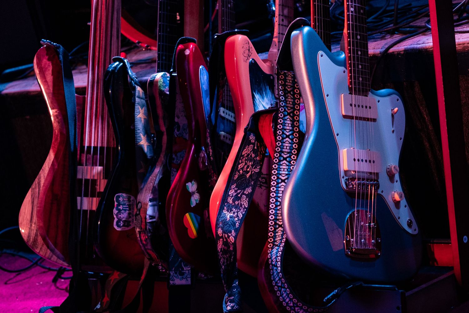 Electric guitars displayed on a wall with dramatic pink and blue lighting creating a moody atmosphere in a music store.
