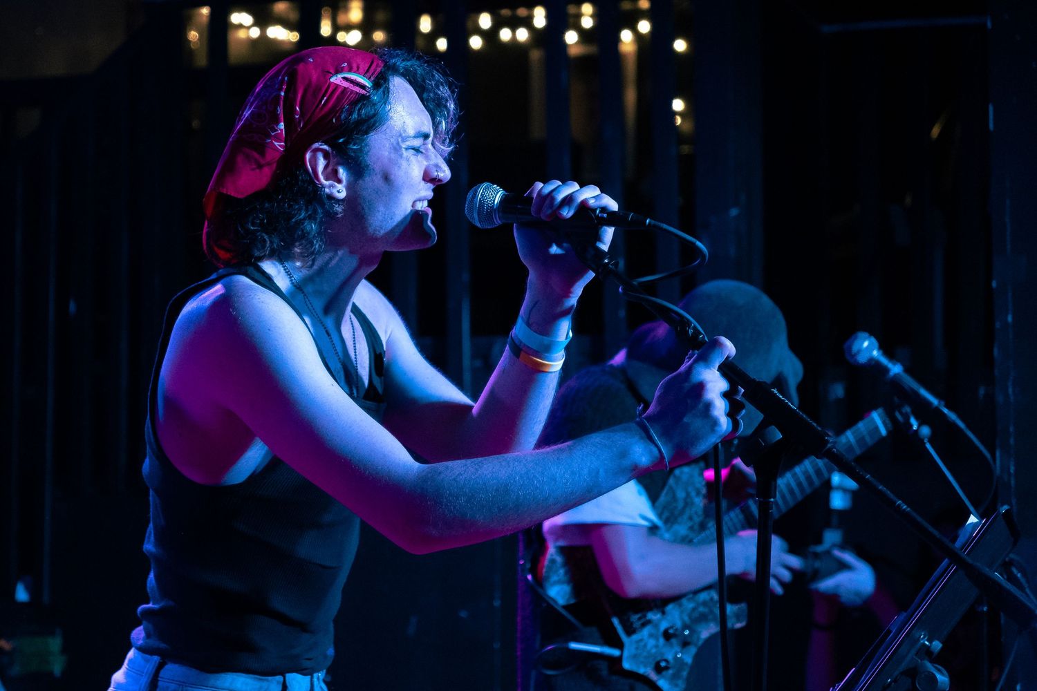 A performer sings passionately on stage illuminated by dramatic blue lighting during a live music performance.