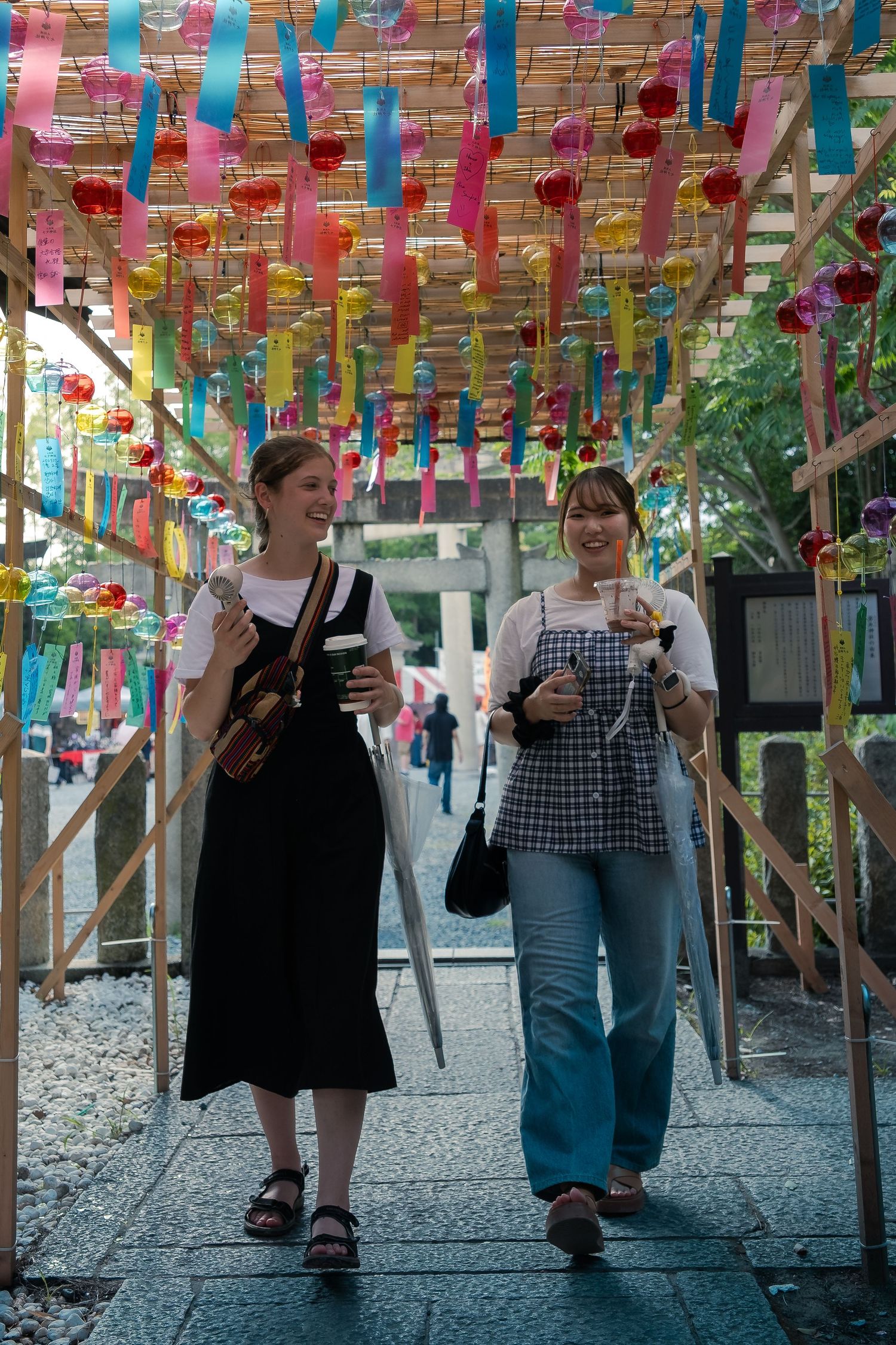 People walk under a vibrant canopy of colorful streamers and decorations at an outdoor festival or celebration.