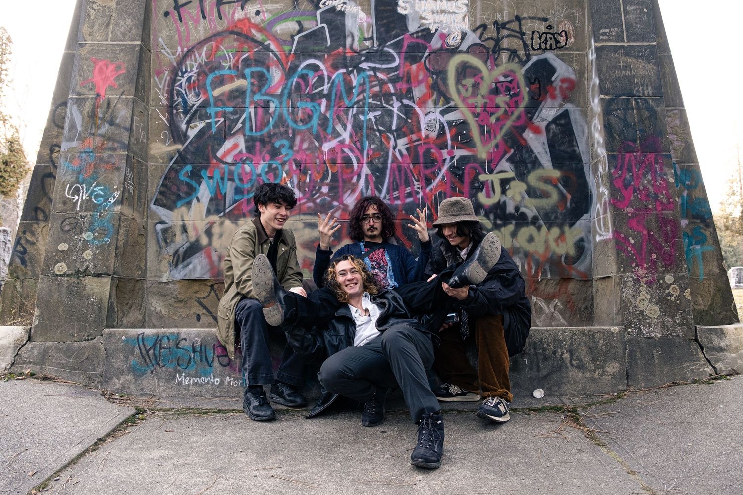 People sitting against a graffiti-covered wall in an urban setting while others stand nearby.