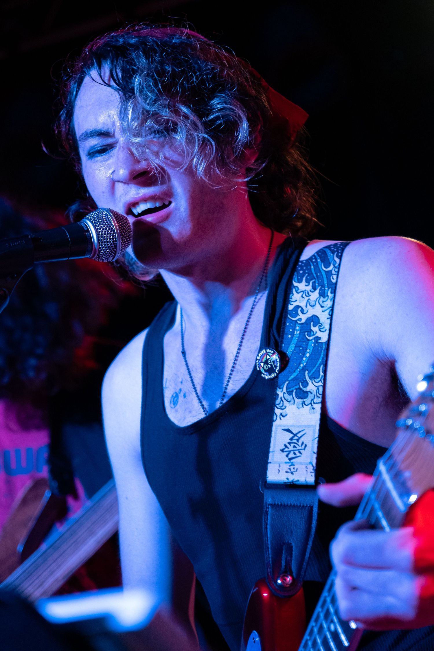 Musician performing on stage with a guitar under dramatic red and blue lighting.