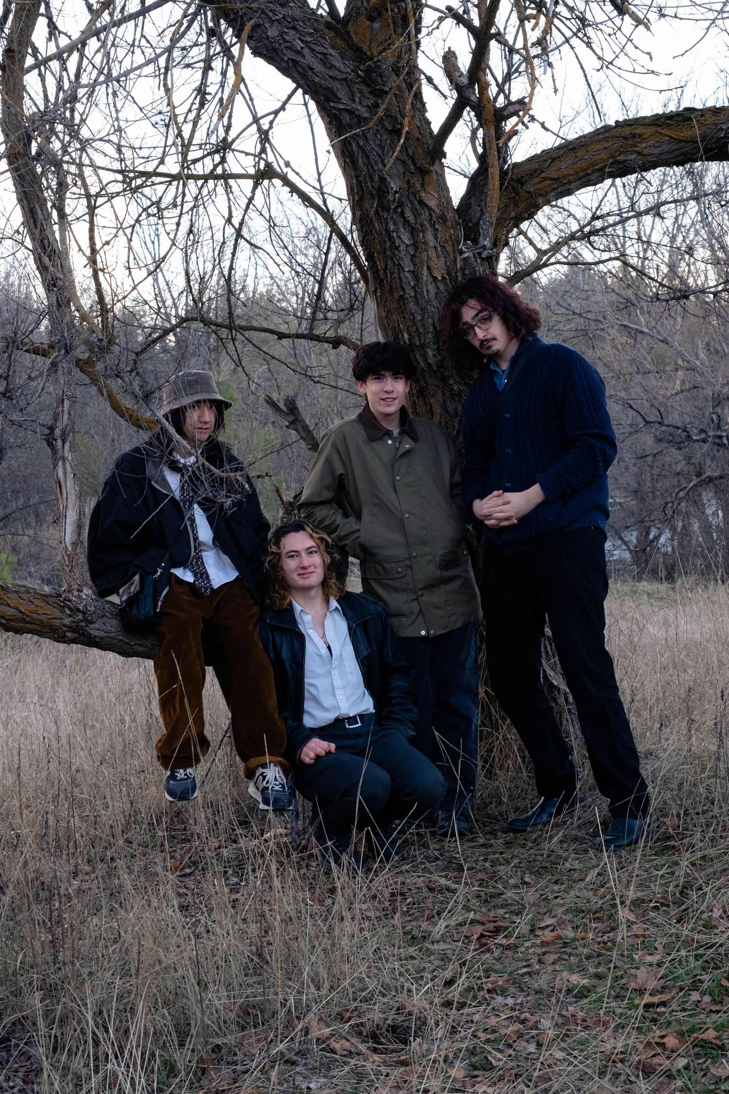 A group poses together under a bare tree in a field of tall brown grass on an overcast day.