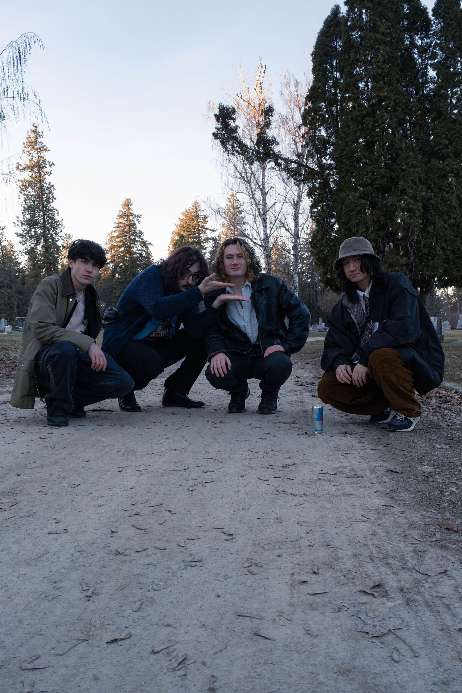 A group of people crouched together on sandy ground with trees visible in the background during sunset.