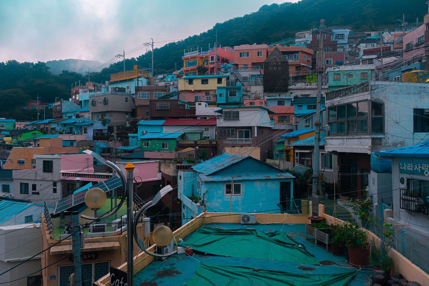 Panoramic view of colorful hillside homes in a coastal town with teal and pink buildings against a cloudy sky.