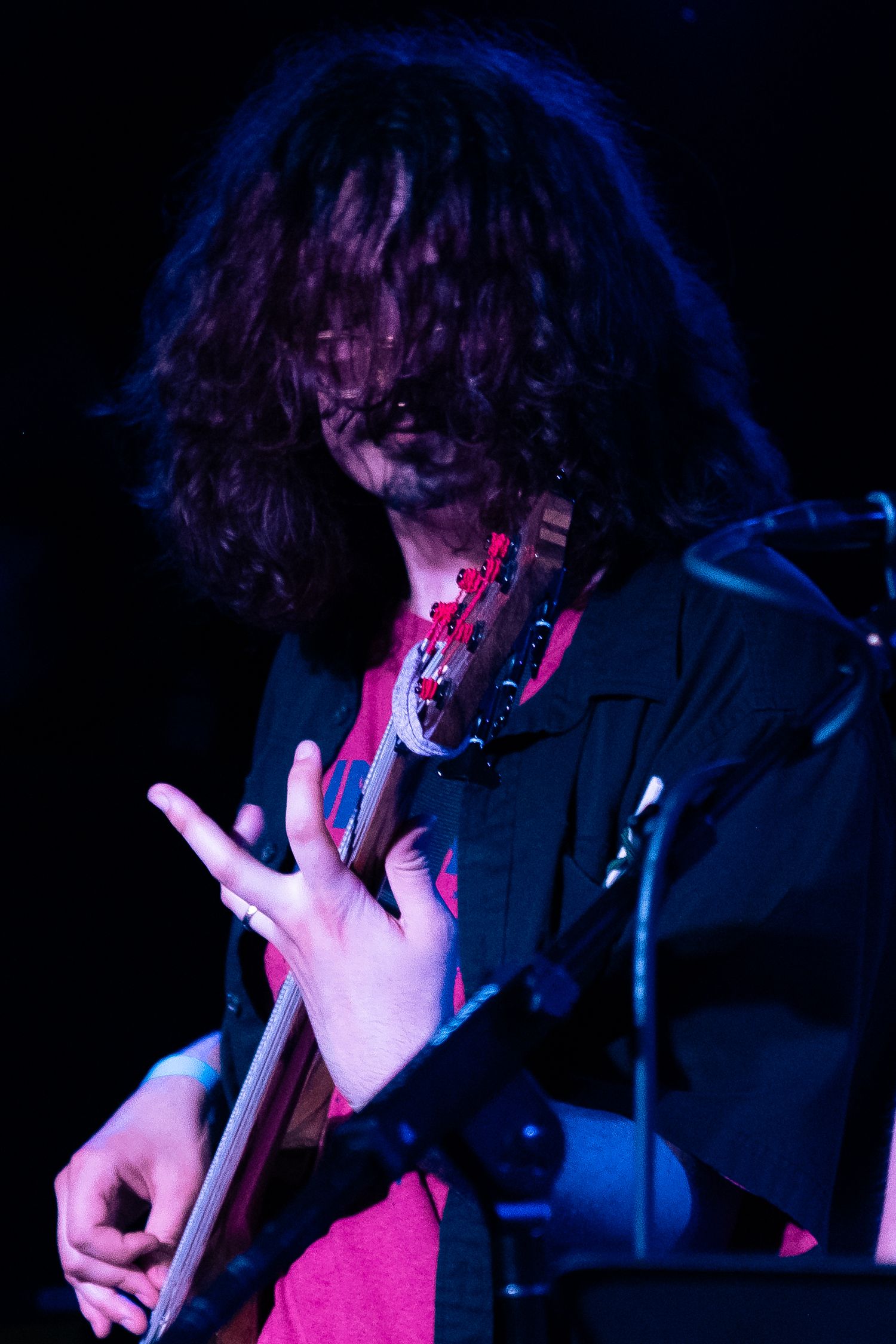 Guitarist performing on stage illuminated by dramatic blue and pink lighting during a live concert performance.