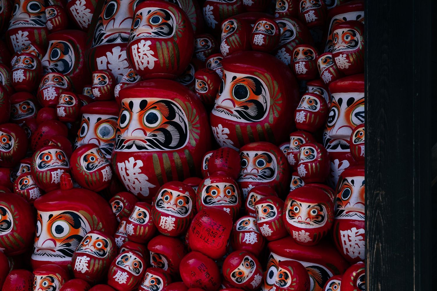 A collection of traditional red Daruma dolls with painted faces stacked together in Japan.