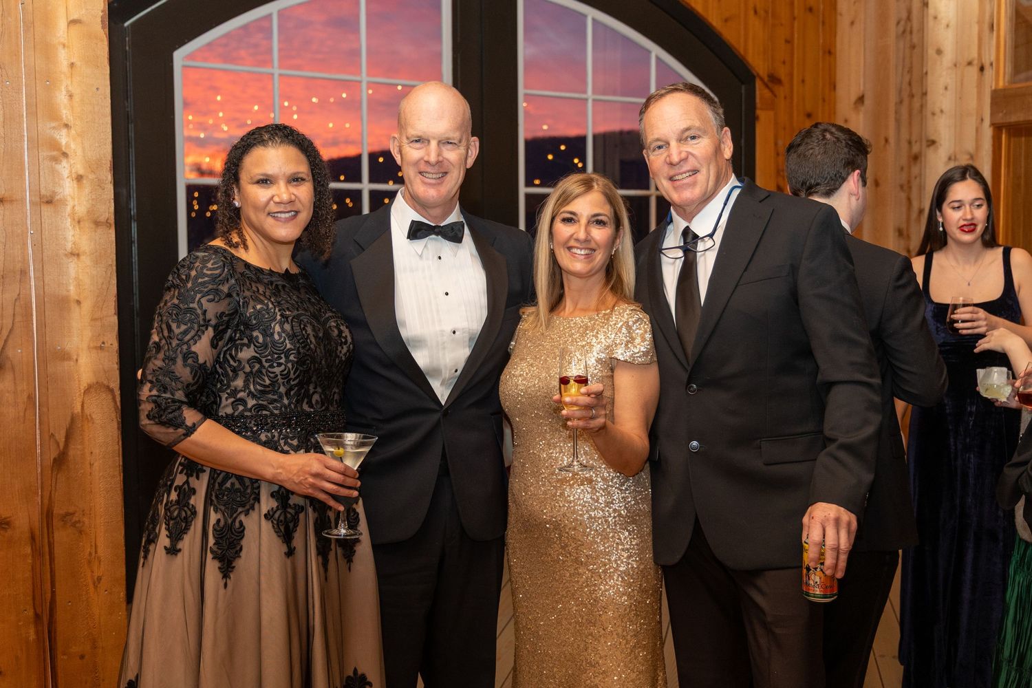 Guests in formal attire socialize and celebrate at an elegant wooden-paneled venue during an evening event.