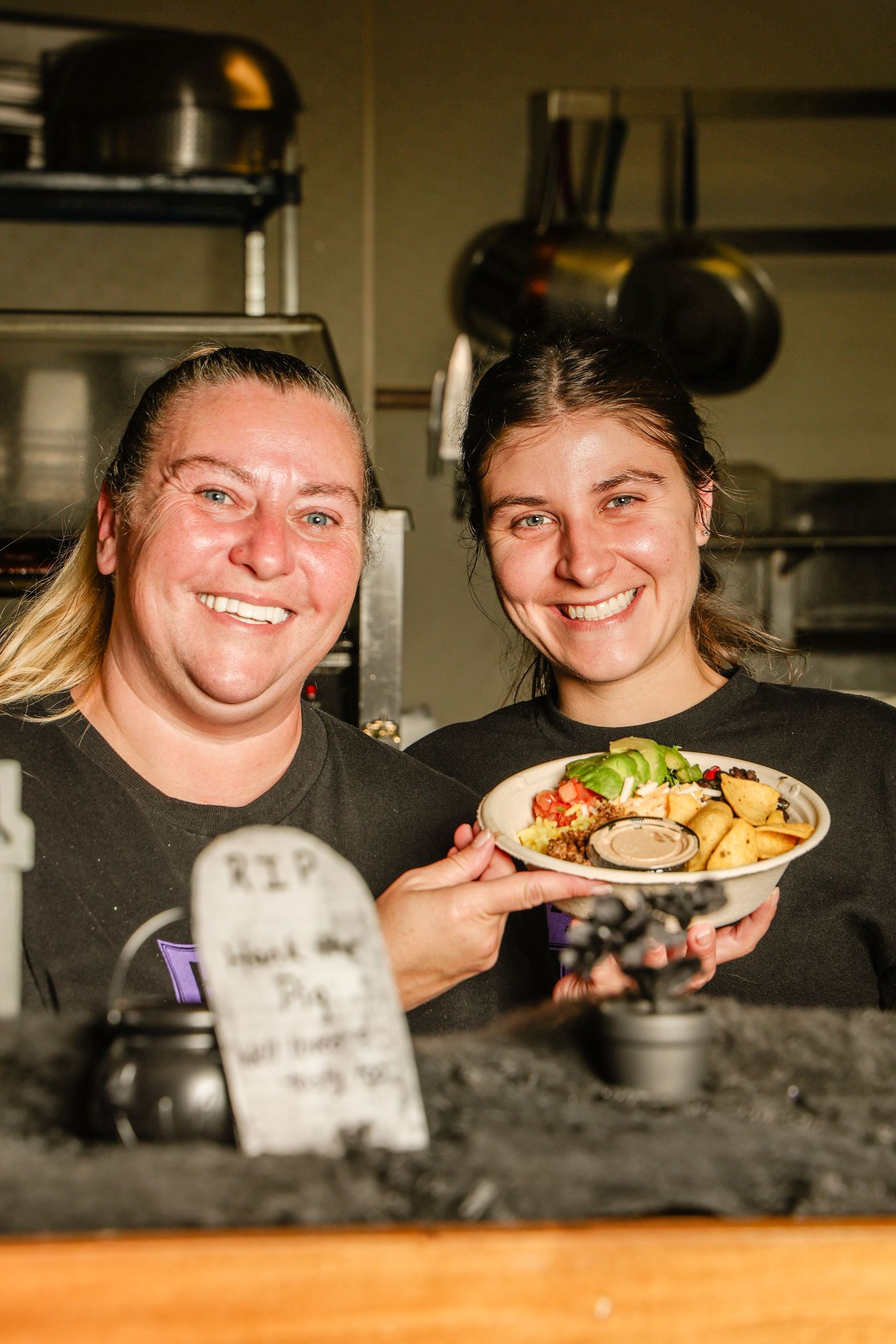 Restaurant staff members smile while holding plates of freshly prepared food behind a kitchen counter.