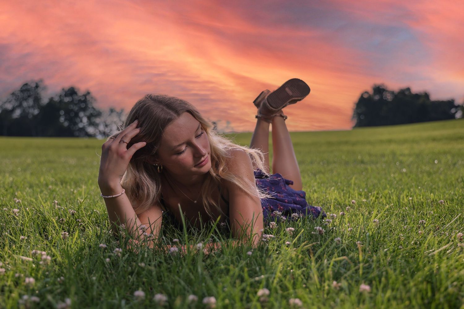Someone relaxes in a lush green field against a vibrant sunset sky with warm orange and pink hues.