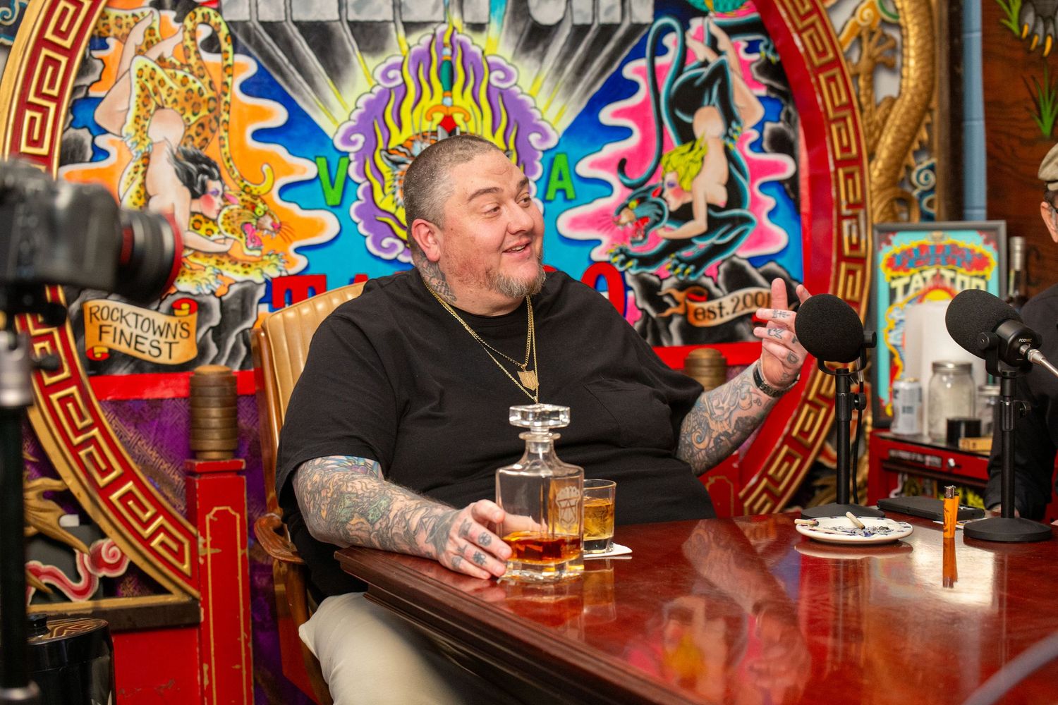 Man with tattoos enjoying beer at colorful bar with artistic mural backdrop.