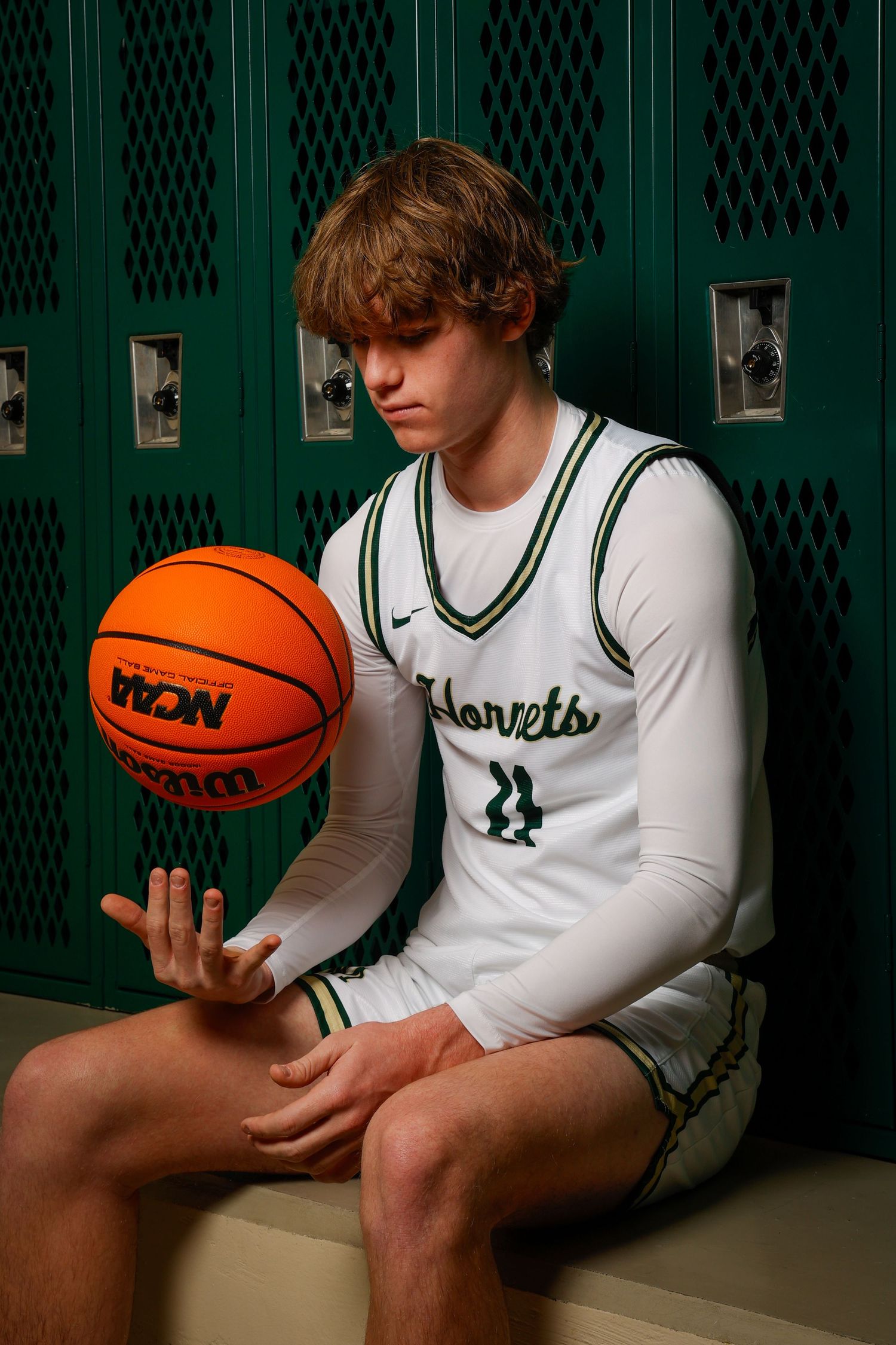 Basketball player sitting in locker room holding orange ball.